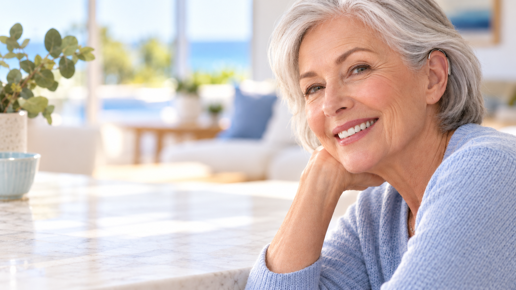 Smiling senior woman wearing a discreet behind-the-ear hearing aid at home.